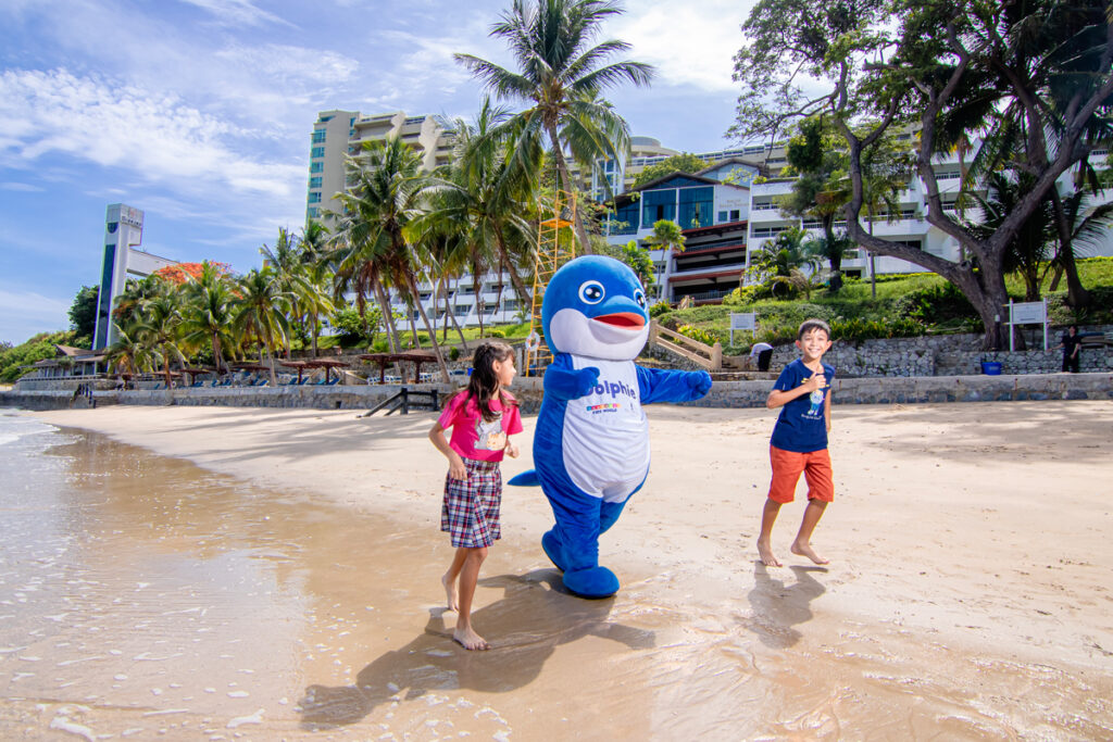 children and dolphin mascot walking on beach at our luxury pattaya hotel